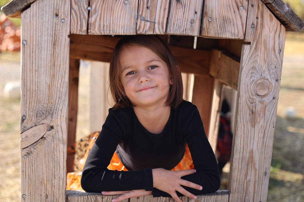 A smiling child enjoying a sunny day, sitting inside a rustic wooden playhouse.