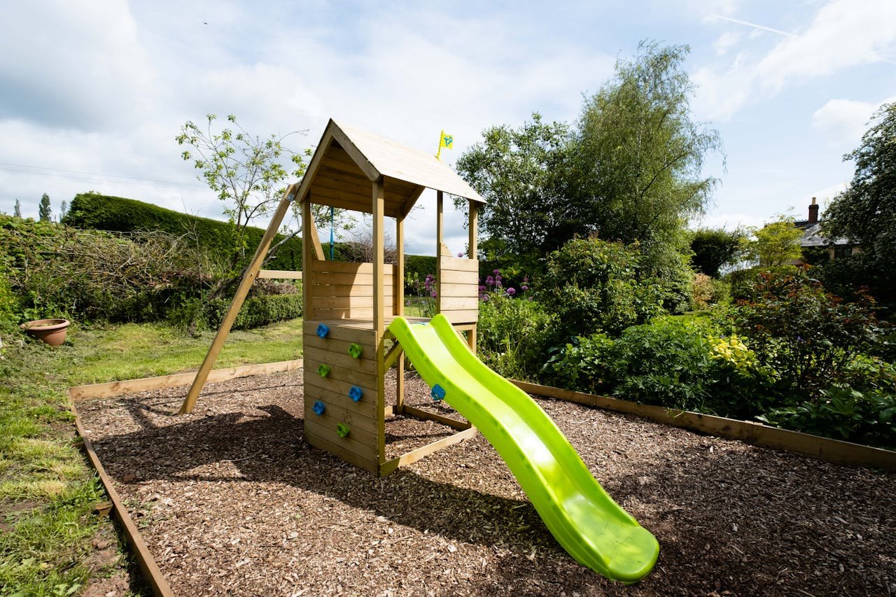 about-img Wooden play structure with slide in a lush garden on a sunny day.
